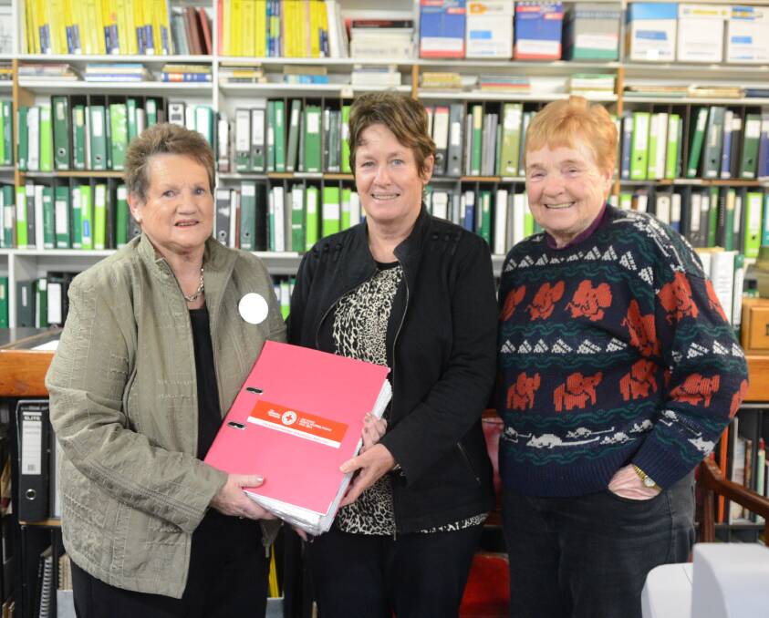 Barbara Hoswell (left) and Wilma Hepburn (right) from Forbes Red Cross deliver the history of the local branch to Kim Smith of Forbes Family History Group.