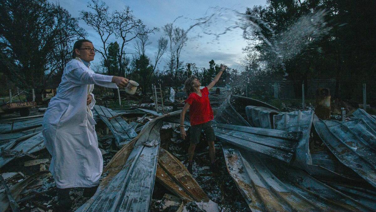 Maz Bruce throws her destroyed diary in the air while Reverend Jude Benton blesses the remains of her house. Photo by Rachel Mounsey